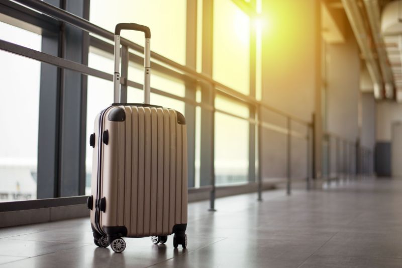 An image of a metallic suitcase sitting alone in a corridor with sun streaming through a window above